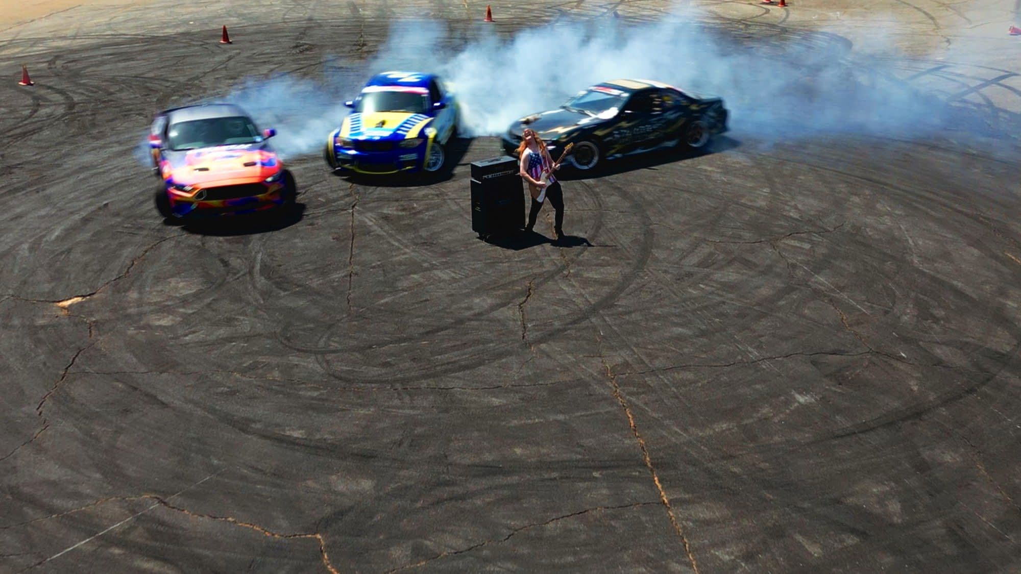 Aerial view of three cars drifting donuts around the guitarist on the SGMP pad