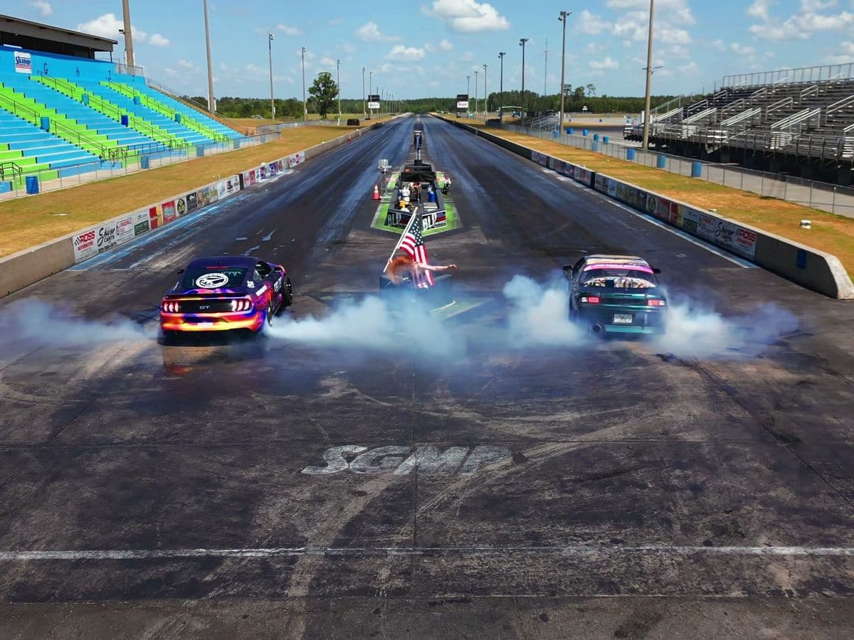 Three cars doing side-by-side burnouts on the SGMP drag strip in front of the grandstands
