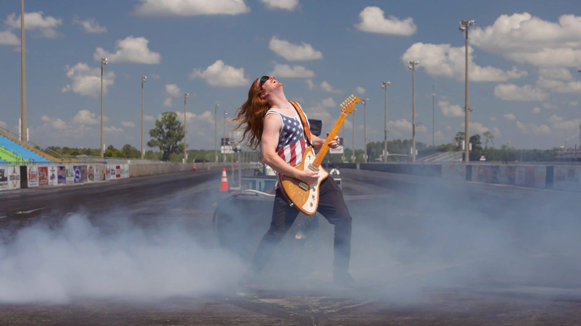A guitarist shredding in the middle of the drag strip at South Georgia Motorsports Park, surrounded by tire smoke